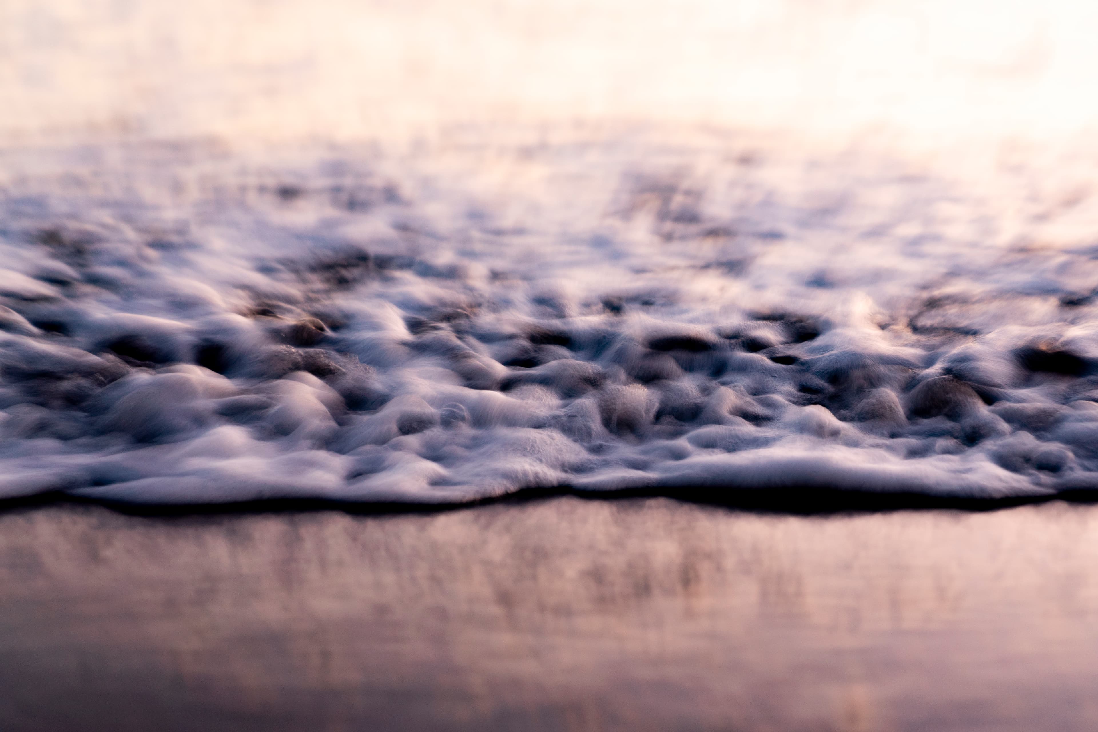 Soft cream sea foam dissolving on pale sand — fine art ocean photography print, Whangamata NZ.