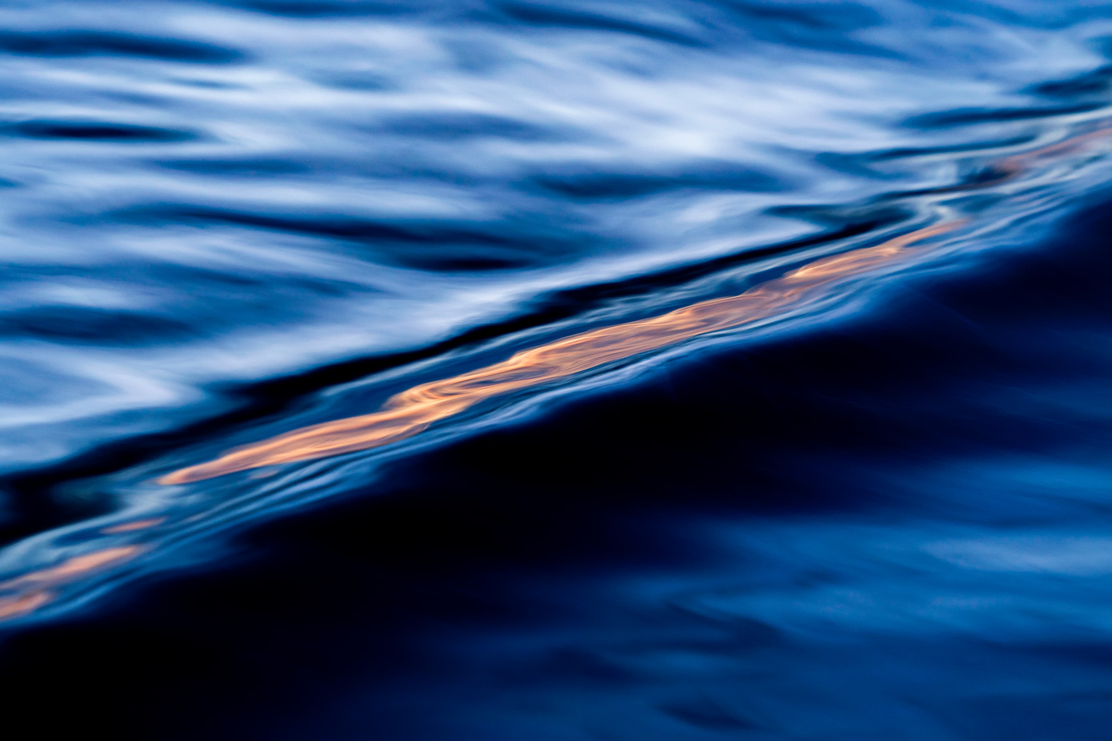 A single golden light streak across a blue wave — fine art ocean photography print, Whangamata NZ.
